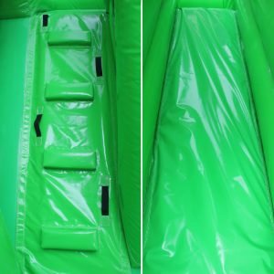 Closeup of a green bouncy castle climbing wall and a slide.